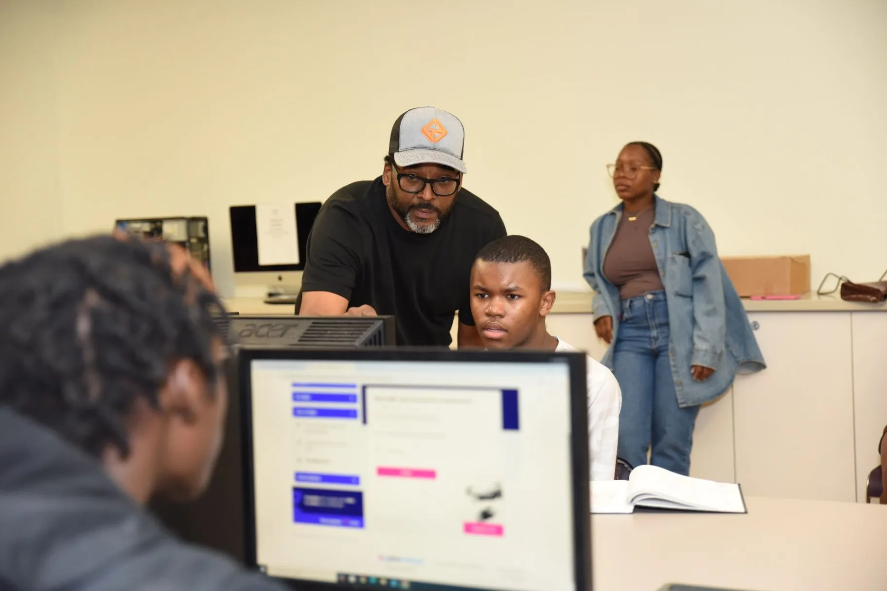 An instructor helping a student at a computer workstation in a classroom